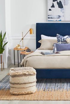 a bed with blue headboard and pillows in a white room next to a painting on the wall