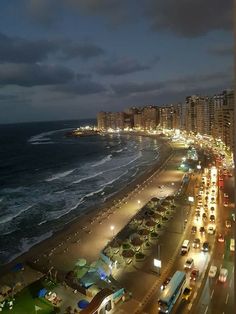 the beach is lit up at night with many cars parked on the shore and buildings in the background