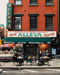 people sitting at tables in front of a restaurant called aleva on the corner of a city street