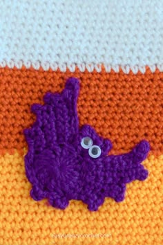 a crocheted purple bat laying on top of an orange and white blanket