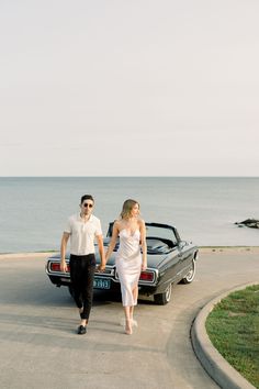 a man and woman walking towards a car by the ocean