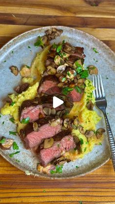 a white plate topped with meat and mushrooms on top of a wooden table next to a fork