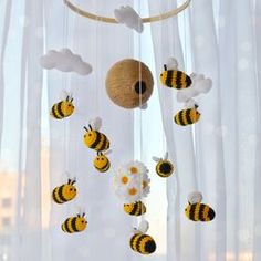 a baby mobile with bees and clouds hanging from it's sides in front of a window