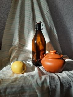 an orange vase sitting on top of a bed next to a brown jug and lemon