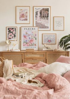 an unmade bed with pink linens and pictures on the wall