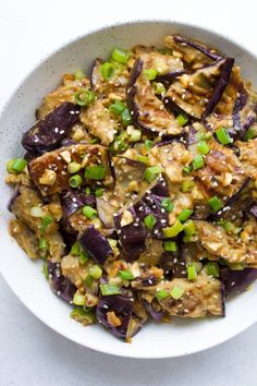 a white bowl filled with eggplant and green onions on top of a table