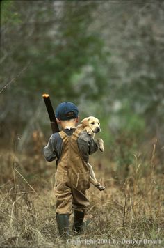 a young boy holding a baseball bat and walking through tall grass with a dog on his back