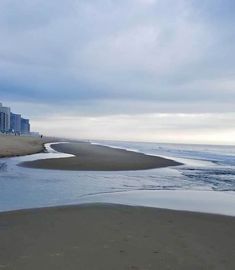 an ocean beach with buildings in the background and water on the sand at the edge