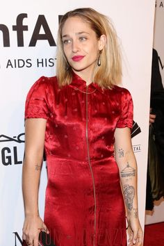 a woman in a red dress with tattoos on her arm and shoulder, standing at an event