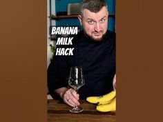 a man sitting at a table with a glass of wine and bananas in front of him