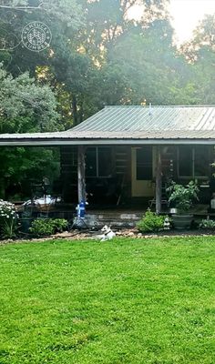 a house with a metal roof in the middle of some grass and trees behind it