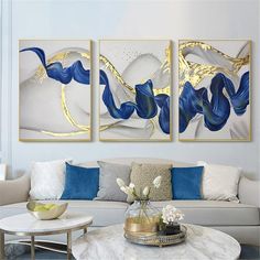 three paintings on the wall above a couch in a living room with white furniture and blue accents