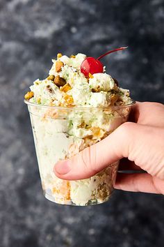 a hand holding up a cup filled with ice cream and toppings on top of it