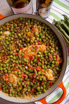 a pan filled with peas and chicken next to a bottle of wine on top of a table