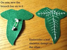 two green leaf brooches sitting on top of a wooden table next to each other