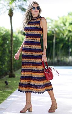 a woman in a multicolored dress is walking down the sidewalk with a handbag