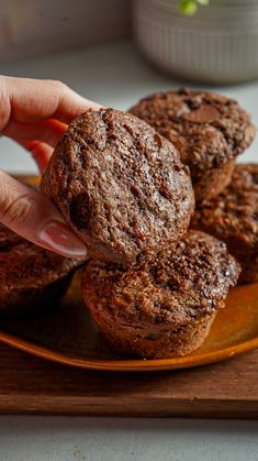 a person picking up some chocolate muffins from a plate on a wooden tray