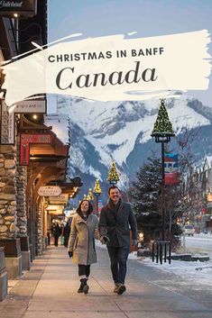 a man and woman walking down a street in front of mountains with the words christmas in banff canada