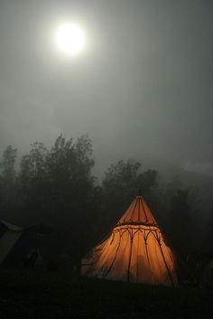 a tent in the dark with trees and fog around it, under a bright sun