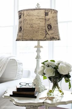 a table with a lamp and some flowers on it in front of a white couch