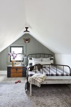 a bedroom with a bed, dresser and window in the atticed room that has an area rug on the floor