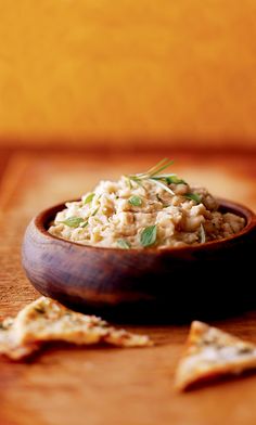 a wooden bowl filled with food sitting on top of a table next to crackers