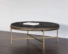 a round coffee table with a gold frame and black velvet upholstered cushion on top