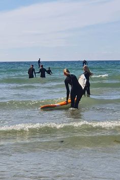 several people in wetsuits are standing in the water with surfboards and one person is holding a surfboard