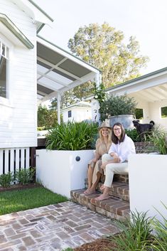 two women are sitting on the steps in front of their house and one is holding her dog