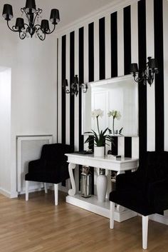 a black and white striped wall in a room with two chairs, a table and a mirror