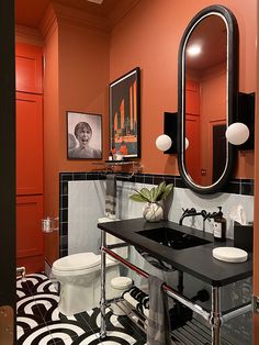 an orange bathroom with black and white tile flooring is pictured in this image, there are two mirrors on the wall above the sink