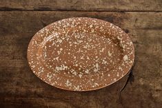 a brown plate with white speckles sitting on top of a wooden table next to a knife and fork