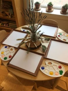 the table is set up with art supplies on it and there are plants in the window sill