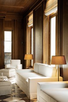 a living room filled with white furniture and wooden paneled walls, along with two lamps on either side of the couches