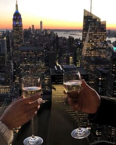 two people toasting with wine glasses in front of the cityscape at sunset