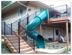 a green slide sitting on top of a wooden deck in front of a house with stairs