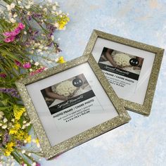 two gold glittered frames with photos in them on a blue background and some flowers