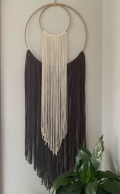 a wall hanging with two circular rings and tassels on the side, next to a potted plant