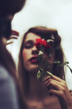 a woman holding a rose up to her face and looking at the camera man's reflection