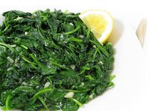 a white plate topped with spinach and lemon wedges