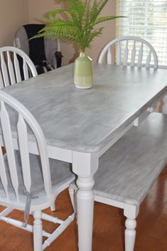 a white table with four chairs and a vase on top of it in a living room