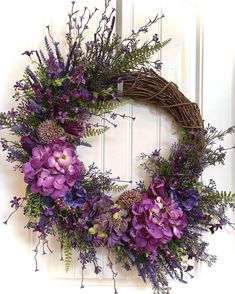 a wreath with purple flowers and greenery hanging on a door