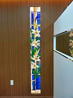 a tall stained glass window in the corner of a room with wood paneling and white flowers