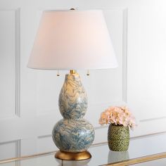 two vases with flowers sit on a glass table next to a lamp that is turned on