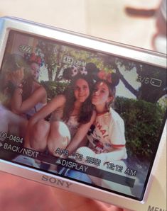 a person holding up a digital camera with two girls on it's screen in front of them