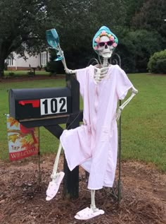 a skeleton dressed in pink stands next to a mailbox