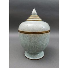 a white vase with gold trimmings and a lid on the bottom is sitting on a gray surface