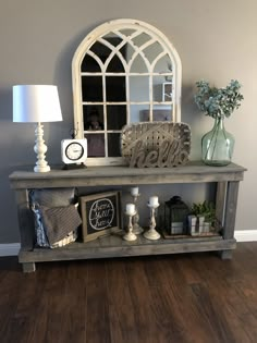 a shelf with candles, mirror and other items on it in front of a gray wall