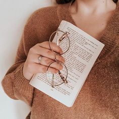 a woman is holding a book and reading glasses on her left hand as she holds it in her right hand