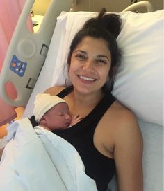 a woman laying in a hospital bed with a baby wrapped up to her chest and smiling at the camera